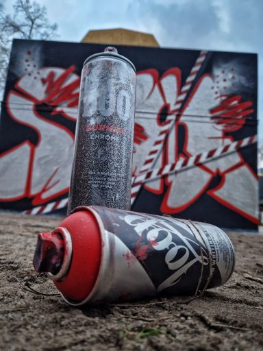 Do not Cross Nahaufnahme von zwei Graffiti-Sprühdosen auf dem Boden im Vordergrund einer bemalten Wand.