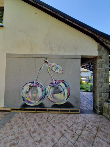 Die bunten Glaskirschen Zwei groß aufgesprühte, metallisch glänzende Kirschen auf einer grauen Wand an einem Gebäude.