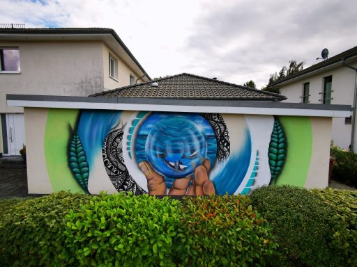 Hausfassade – Glaskugel & Naturmotive Modernes Mural auf einer Garagenwand mit Händen, die eine magische Glaskugel mit Walen halten, umgeben von grünen Blättern.