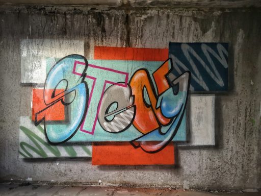 Mosaik Graffiti Auf eine Betonwand gesprühter Graffiti-Schriftzug Stay in Blau und Orange.