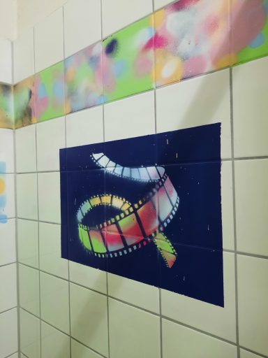 Filmkunst auf Fliesen Eine Nahaufnahme von weißen Fliesen, auf denen ein kleiner, bunter Filmstreifen mit einem Graffiti-Herz und einem Smiley aufgesprüht ist.