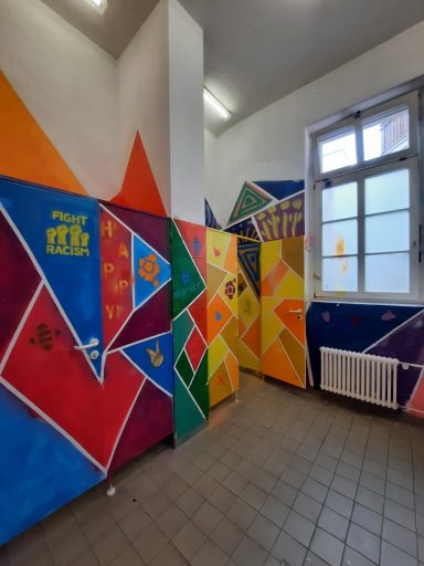 Bunter Schultoiletten-Flur Ein Toilettenraum mit Toilettentüren, die in bunten geometrischen Mustern bemalt sind. Ein Schriftzug an der Wand ruft zu Gleichheit auf.