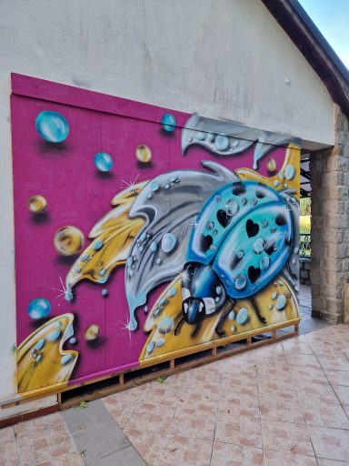 Marienkäfer Luxusedition Bunte Graffiti-Darstellung eines stilisierten Marienkäfers auf einer rosa Wandfläche.