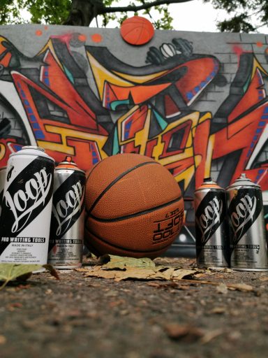 Basketball und Sprühdosen Stillleben Ein Basketball und verschiedene Sprühdosen liegen auf dem Boden vor einem Graffiti.
