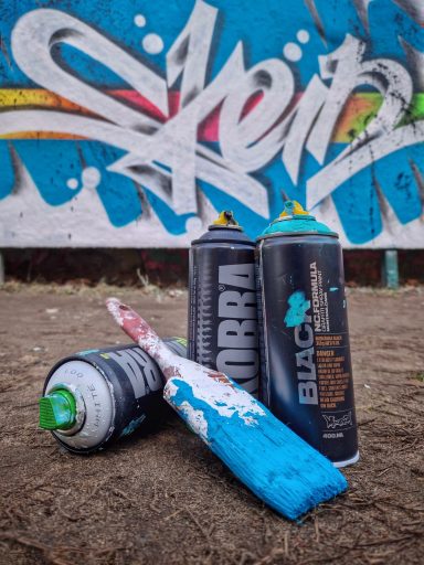 Die Waffen der Wahl Nahaufnahme von zwei Spraydosen auf einer Mauer vor einer bunten Graffiti-Wand.