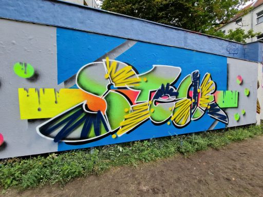 Neon-Sten Buntes, großflächiges Graffiti in Gelb und Blau auf der Wand eines flachen Gebäudes.