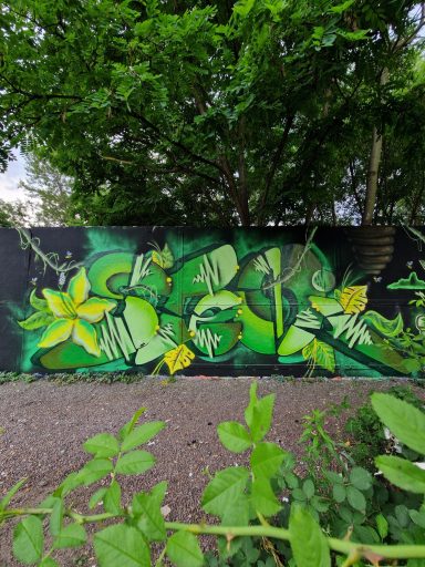 Junglequeen Grünes Graffiti mit floralen Mustern und Blüten an einer Wand vor grünem Hintergrund.