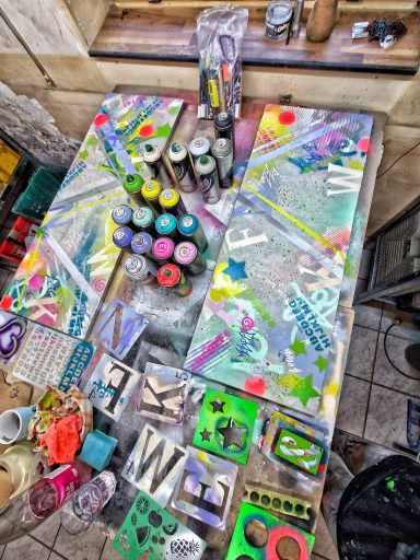 Bunte Holzleinwände und Spraydosen Draufsicht auf farbig besprühte Holzbretter, Kunsthandwerk und sortierte Spraydosen auf einem Arbeitstisch.