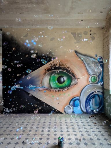 Green Eye Serie Ein großes grünes Auge im Fokus eines surrealen Wandgemäldes mit Wassertropfen und kosmischen Elementen.