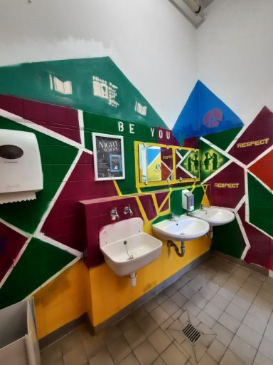 Farbenfroher Waschraum Ein farbenfroher Toilettenbereich mit gelben Waschbecken, bunten Spiegelrahmen und einer Mosaikwand.