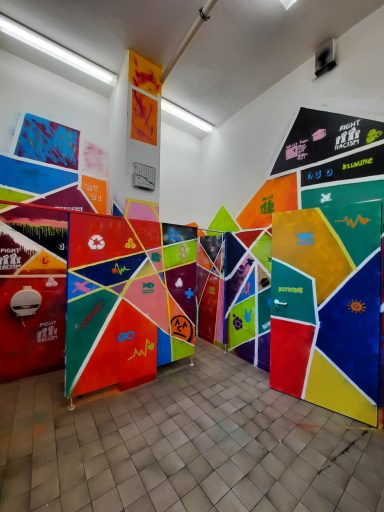 Geometrisches Toiletten-Labyrinth Ein Gang in einem Toilettenbereich, der von Trennwänden mit bunten geometrischen Mustern gesäumt ist.