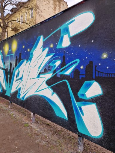 Blaues Nightlife Skyline Graffiti Blau-weißes Graffiti auf einer Gebäudewand mit einer nächtlichen Skyline im Hintergrund.